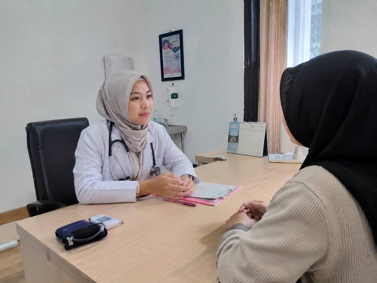 Dokter sedang berkonsultasi dengan pasien di ruang klinik untuk membahas kesehatan dan menjaga kerahasiaan data pasien.